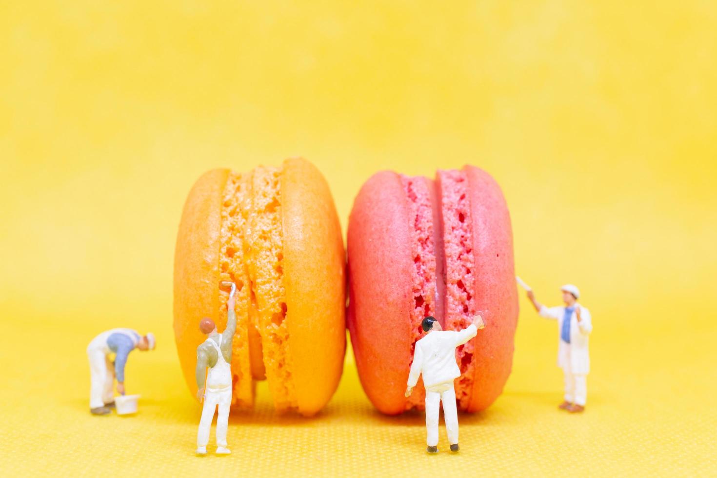Miniature painters coloring macaroons on a yellow background photo