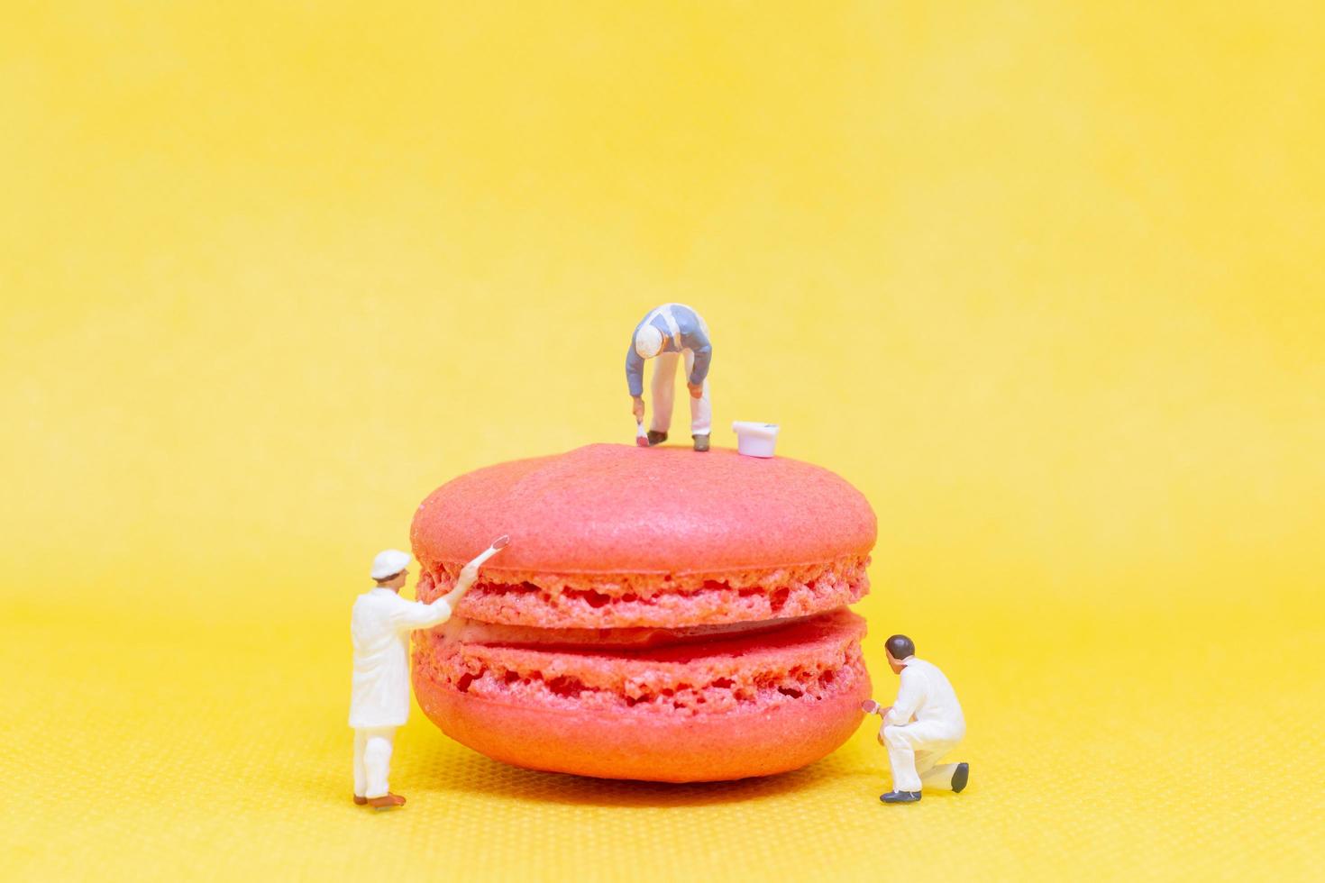 Miniature painters coloring macaroons on a yellow background photo