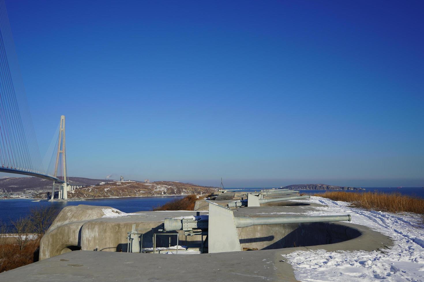 Landscape view of the Voroshilov battery and the Russky Bridge against a clear blue sky in Vladivostok, Russia photo