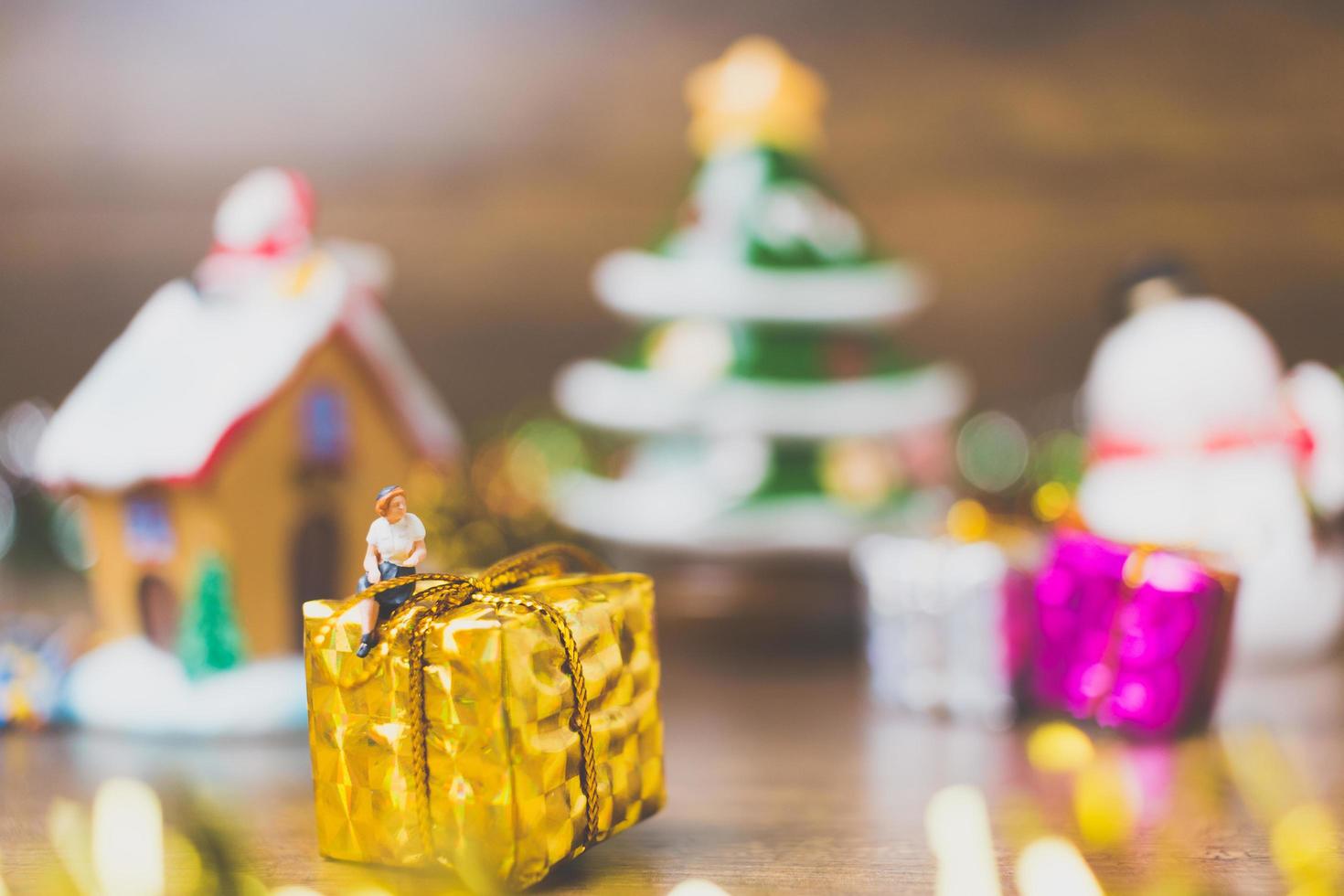 Miniature person on a gift box with Christmas celebration decoration in the background photo