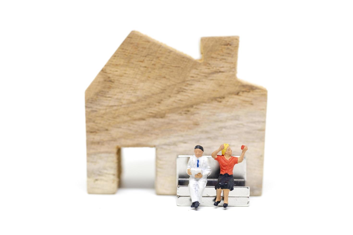 Miniature husband and wife sitting in front of a house on a white background, family concept photo