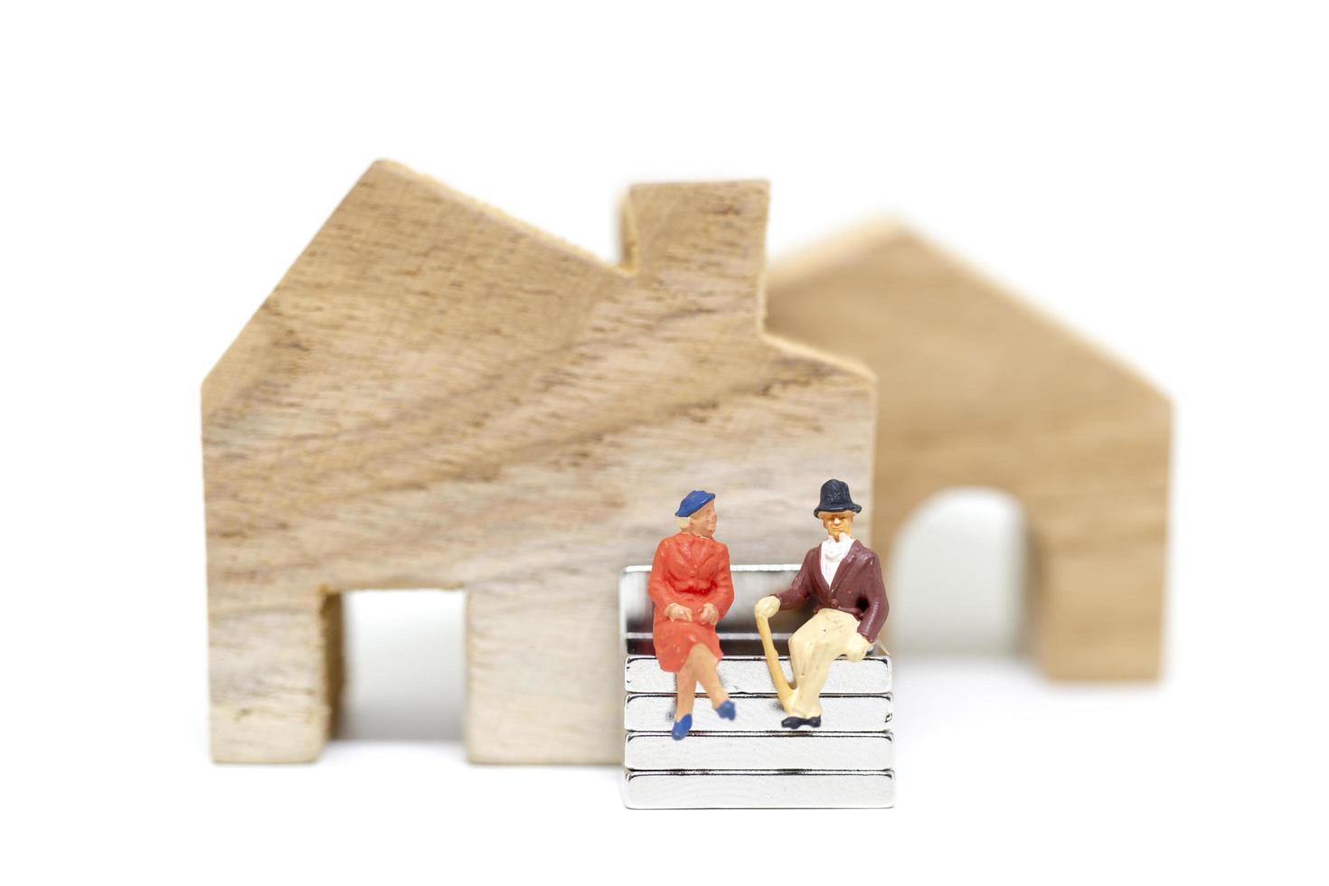Marido y mujer en miniatura sentados delante de una casa sobre un fondo blanco, concepto de familia foto