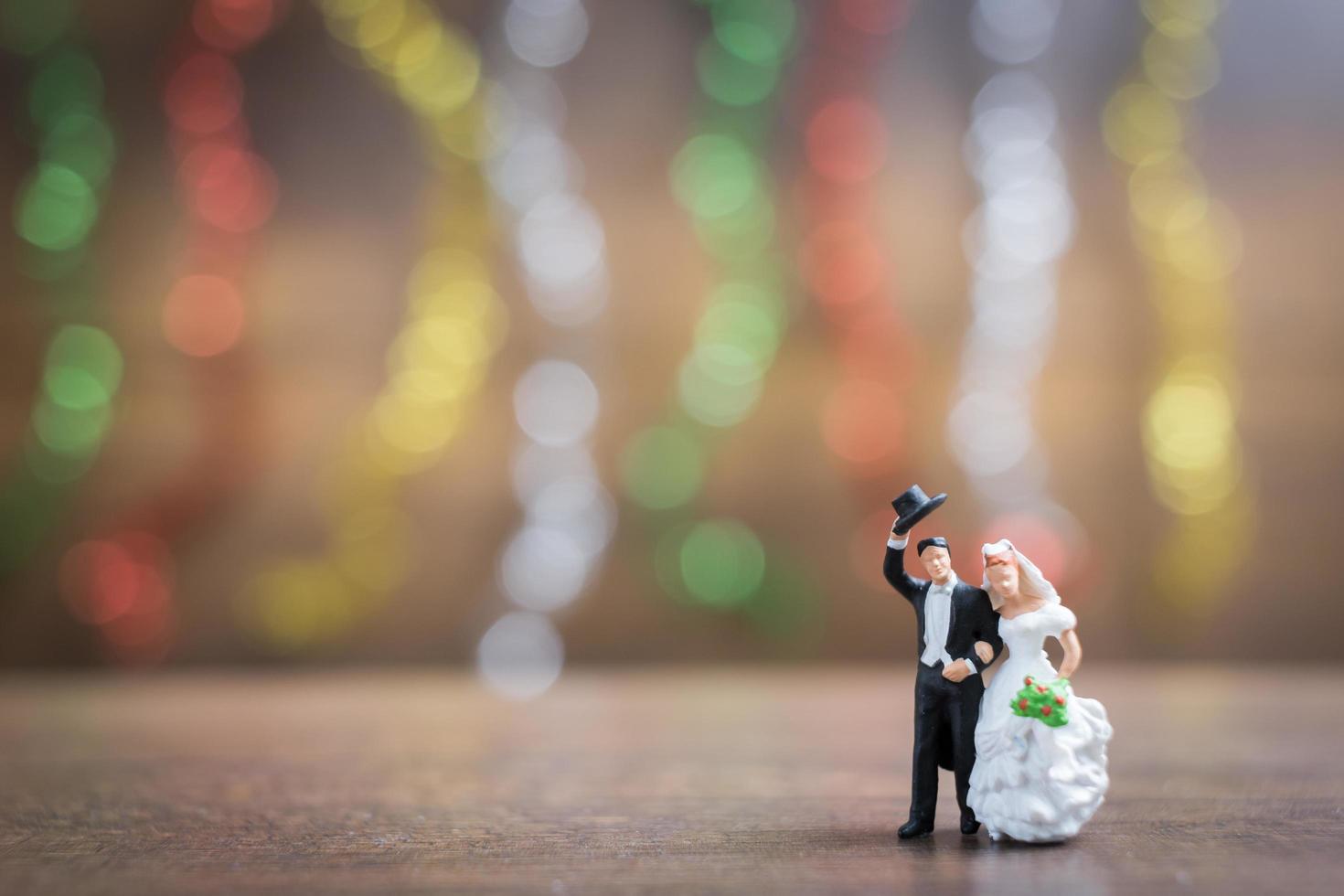 Miniature bride and groom on a wooden floor with colorful bokeh background, successful family concept photo