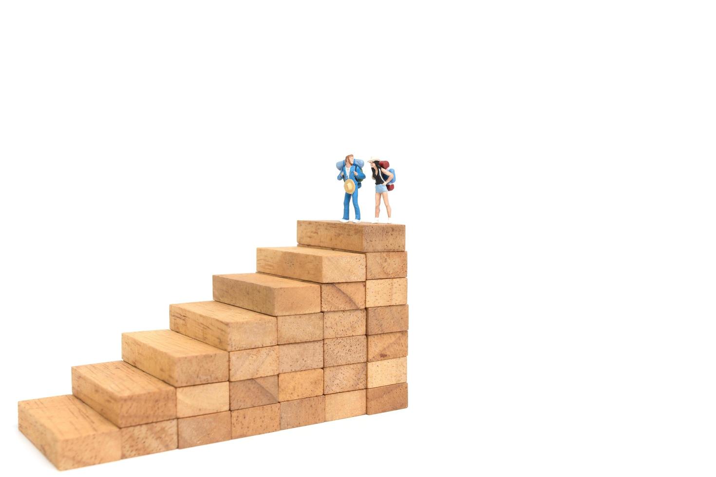 Miniature backpackers standing on wood blocks isolated on a white background, travel concept photo