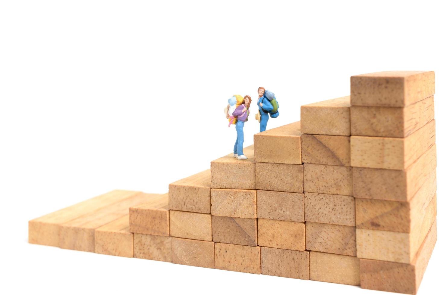 Miniature backpackers standing on wood blocks isolated on a white background, travel concept photo