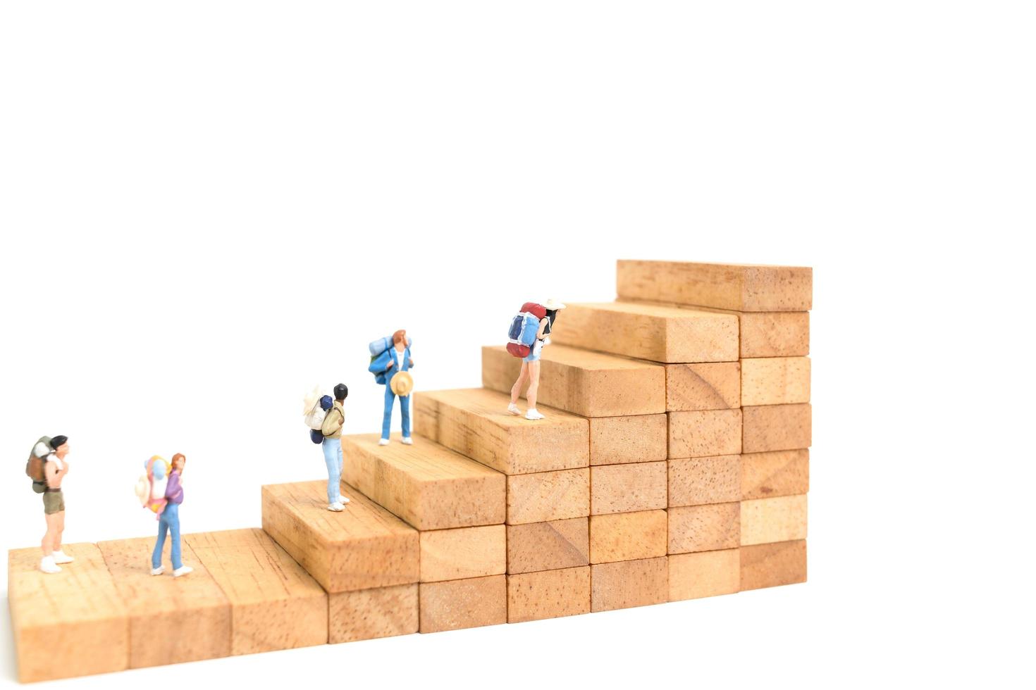 Miniature backpackers standing on wood blocks isolated on a white background, travel concept photo
