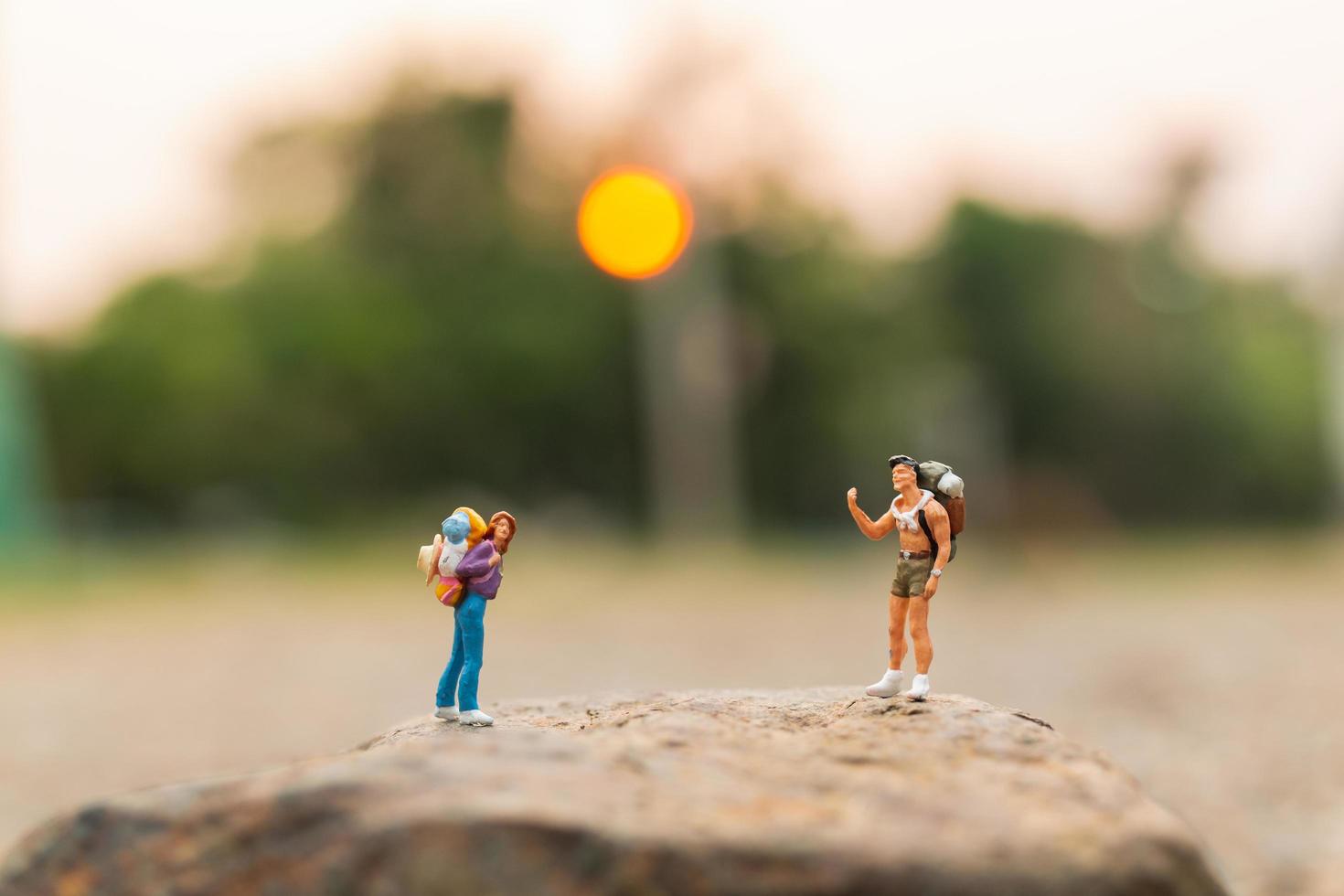 Viajeros en miniatura con mochilas caminando sobre una roca, concepto de viaje y aventura foto