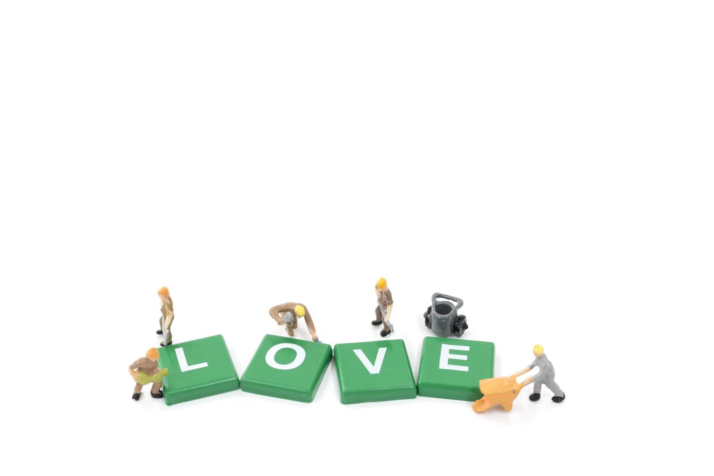 Miniature workers building the word love on a white background photo