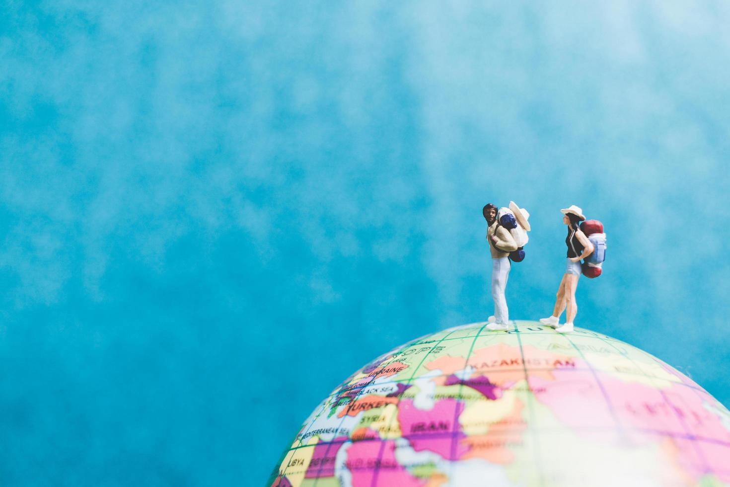 Miniature travelers with backpacks standing on a world globe and walking to a destination photo