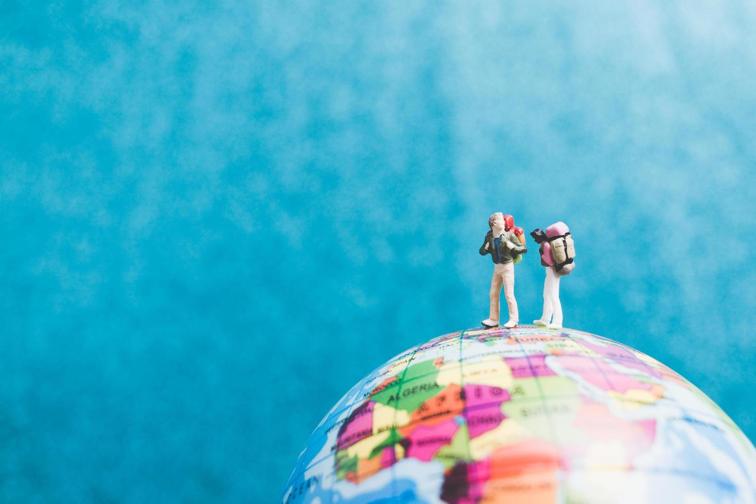 Viajeros en miniatura con mochilas de pie sobre un globo terráqueo y caminando hacia un destino. foto