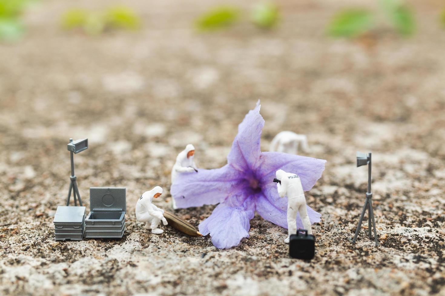 Policía y detective en miniatura encontrando pruebas de una flor en la escena del crimen foto