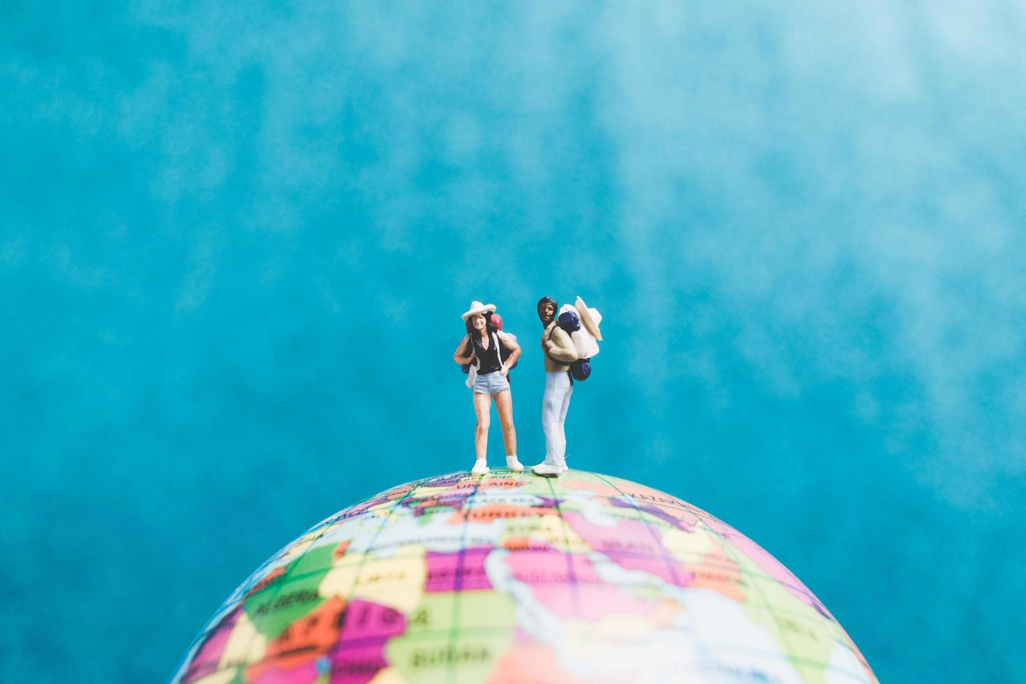 Miniature travelers with backpacks standing on a world globe and walking to a destination photo