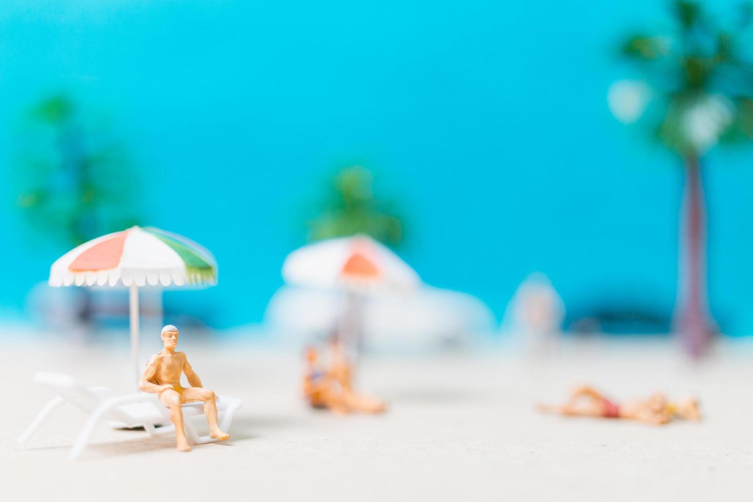 Gente en miniatura vistiendo trajes de baño relajándose en una playa, concepto de verano foto