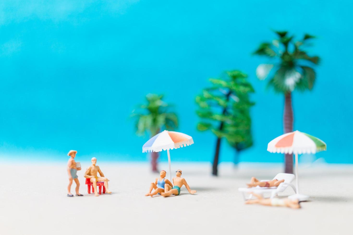 Miniature people wearing swimsuits relaxing on a beach, summer concept photo