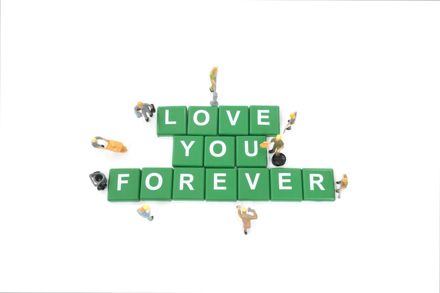 Miniature workers building the words love you forever on a white background photo