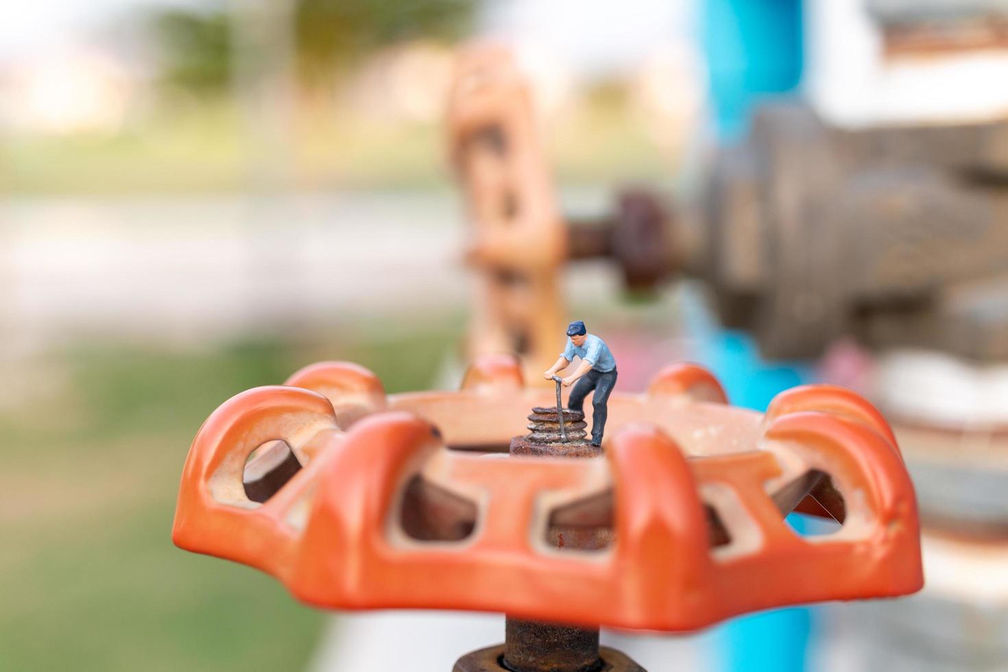 Plomero en miniatura instalando tuberías de agua y comprobando daños en una máquina bomba de agua foto