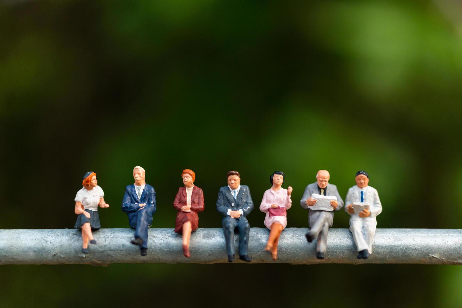 Miniature businesspeople sitting on a wire with a green background, business team concept photo