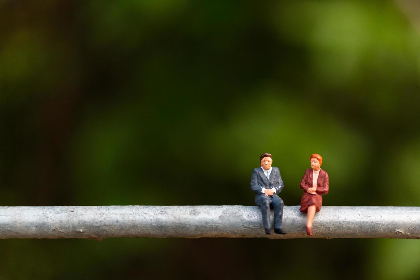 Miniature businesspeople sitting on a wire with a green background, business team concept photo