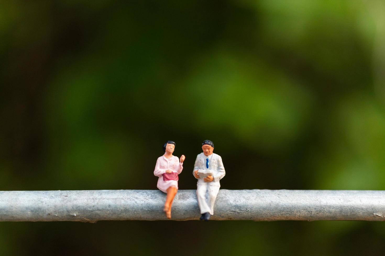 Miniature businesspeople sitting on a wire with a green background, business team concept photo