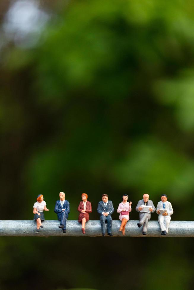 Miniature businesspeople sitting on a wire with a green background, business team concept photo