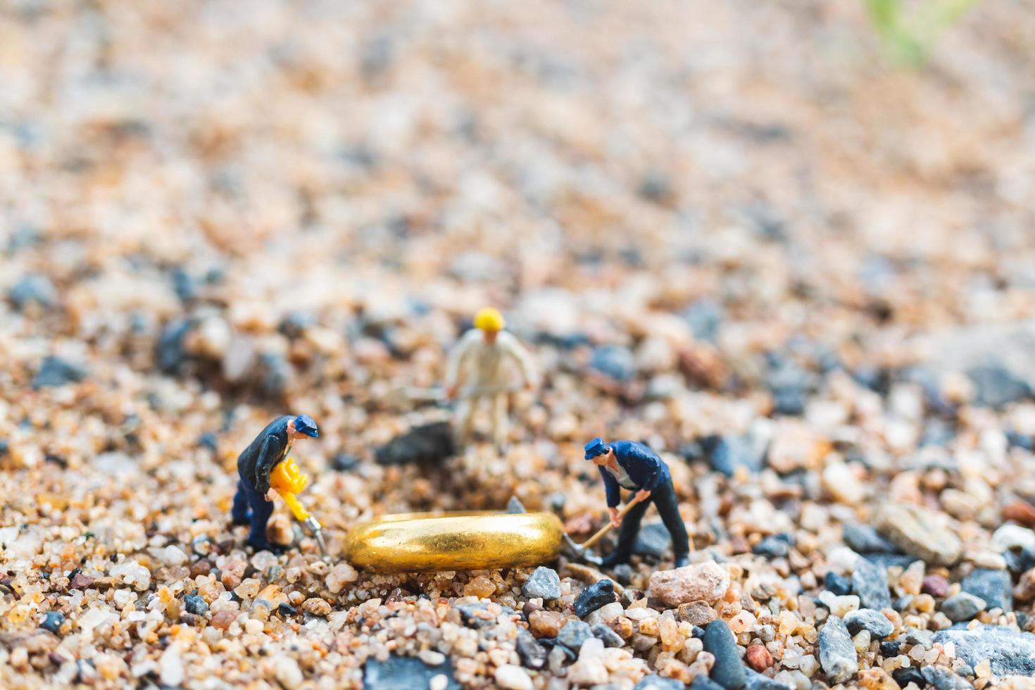 Trabajadores en miniatura cavando anillos de oro en la arena, concepto de crecimiento empresarial foto