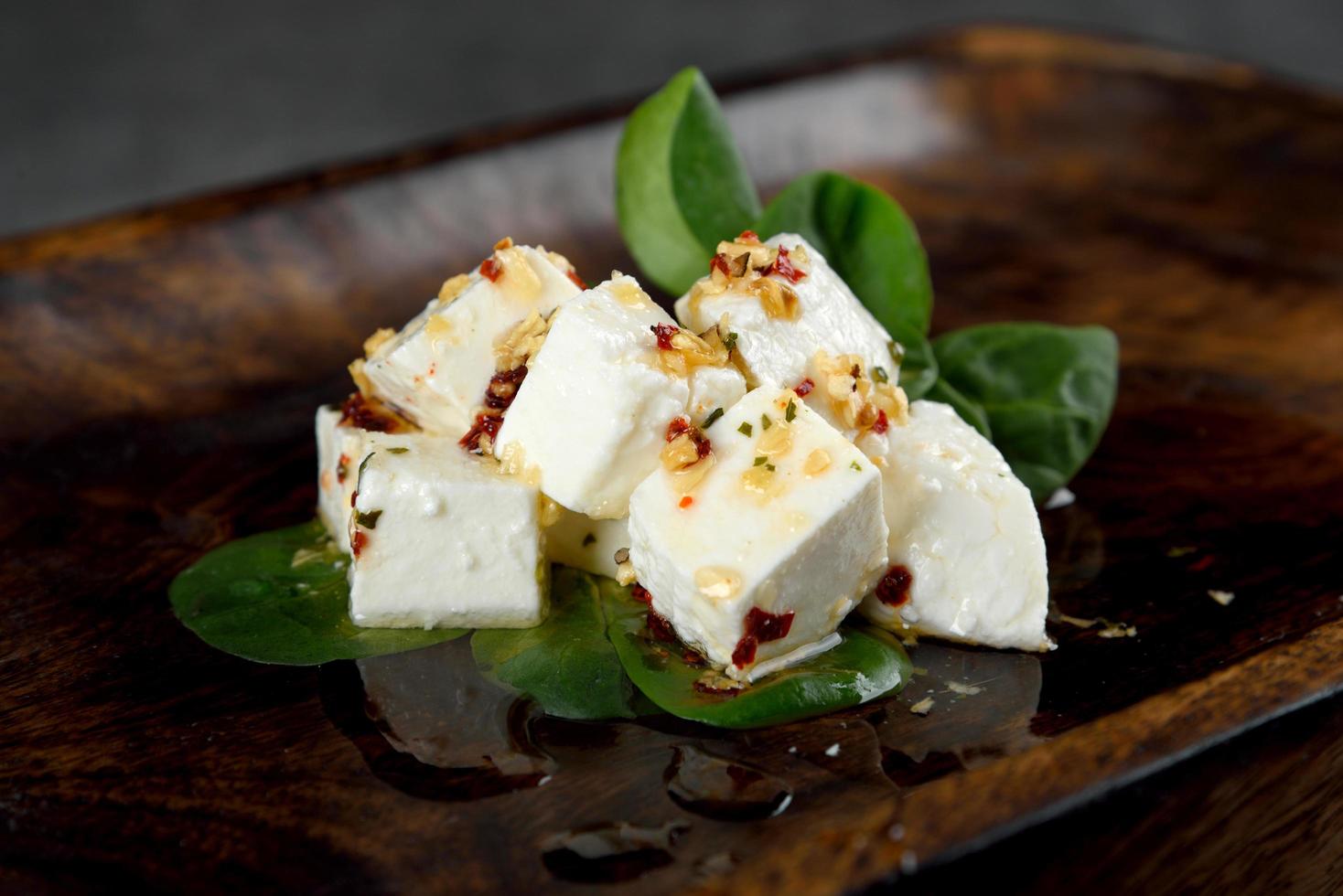 Queso feta servido con verduras frescas sobre fondo de madera oscura. foto