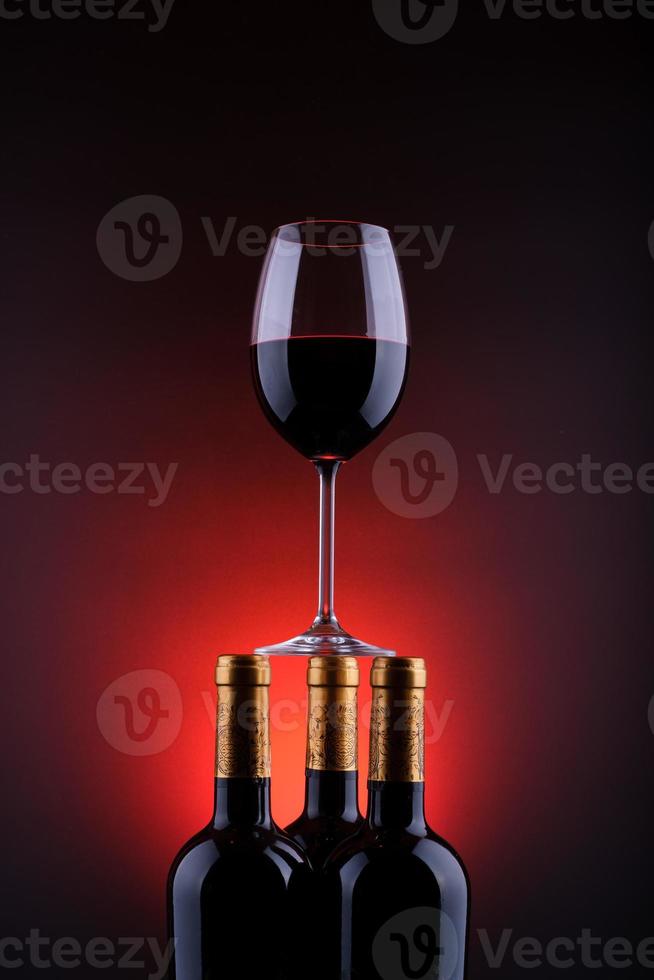 Botellas de vino y vaso lleno con fondo rojo y negro. foto