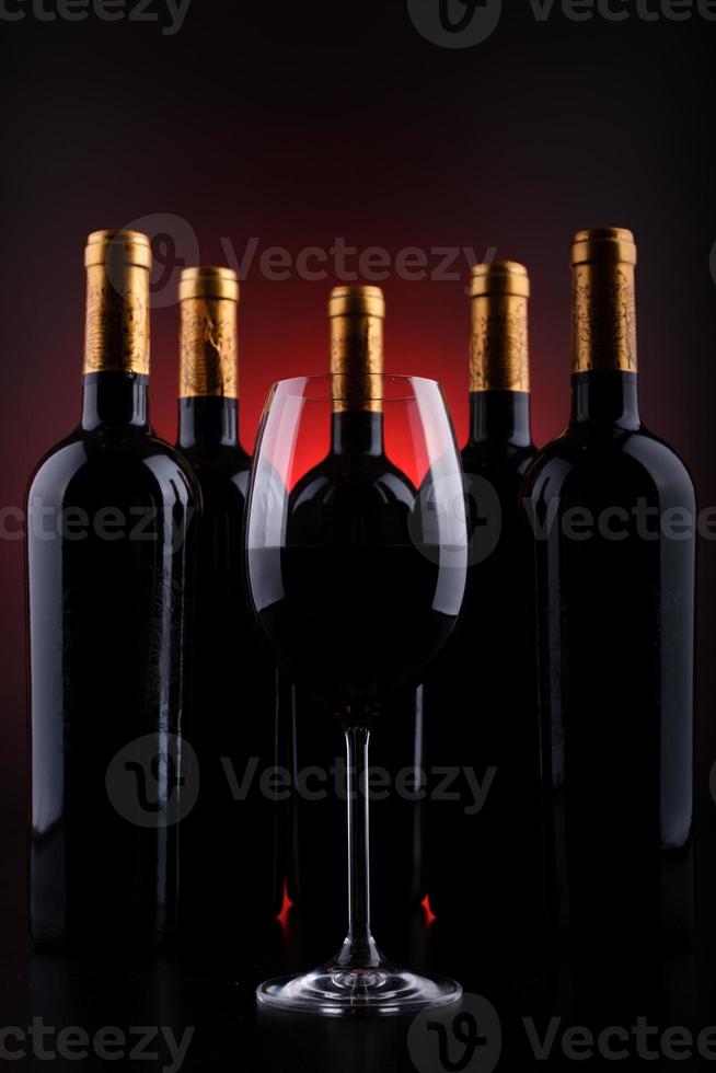 Botellas de vino y vaso lleno con fondo rojo y negro. foto