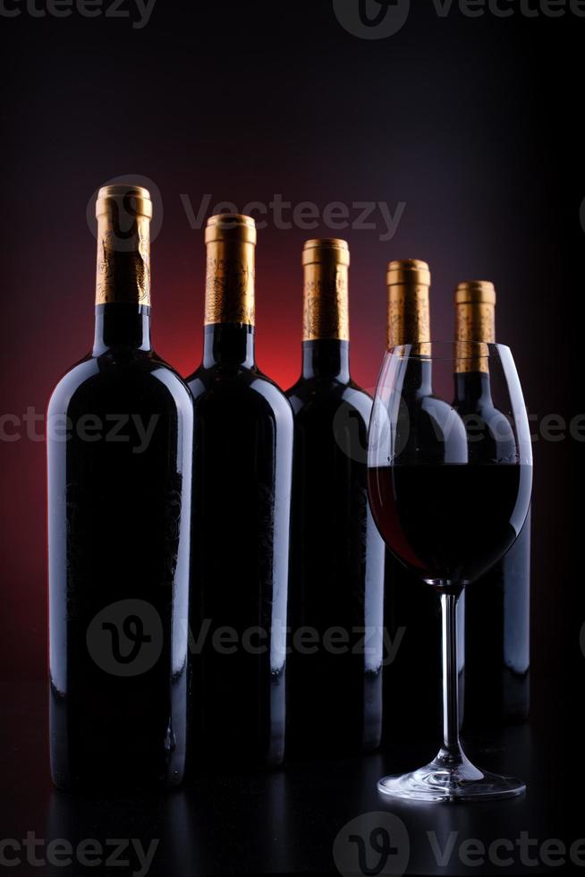 Botellas de vino y vaso lleno con fondo rojo y negro. foto