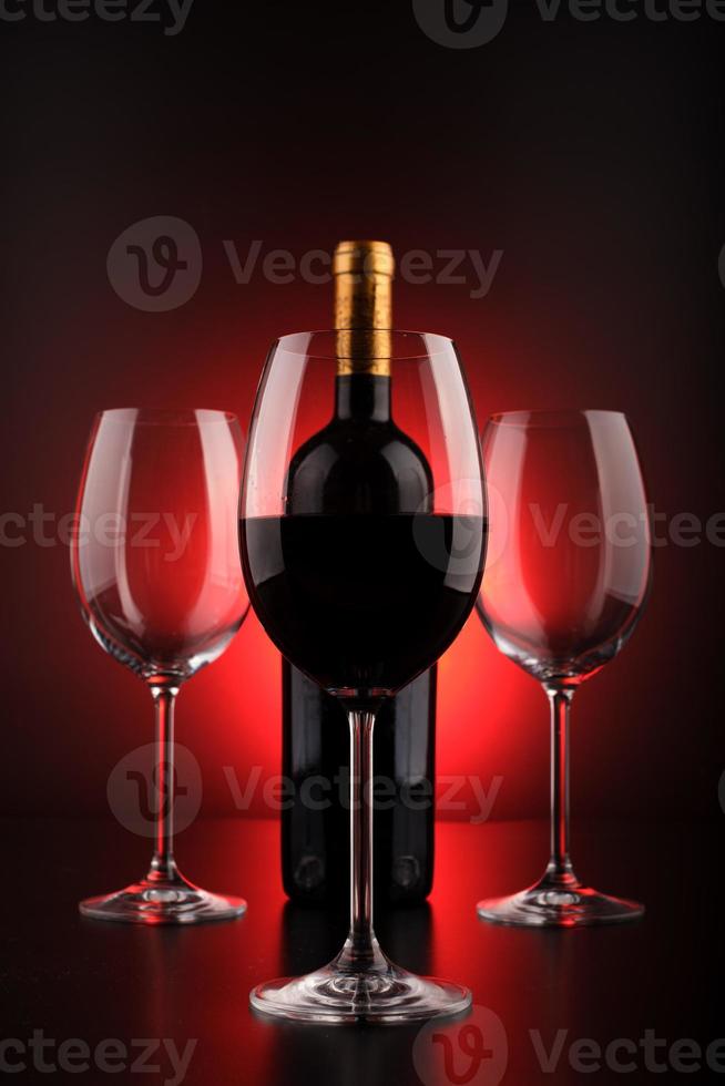 Botellas de vino y vaso lleno con fondo rojo y negro. foto