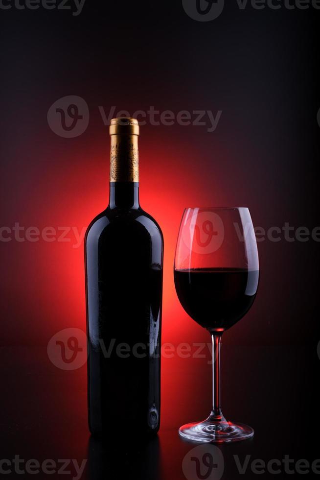 Wine bottle with full glass black background and red photo