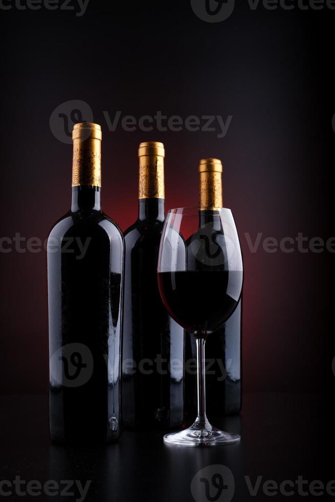 Botellas de vino y vaso lleno con fondo rojo y negro. foto