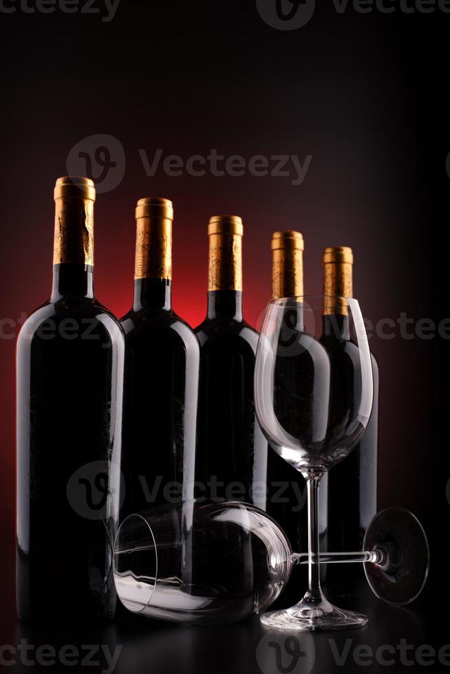 Botellas de vino y vasos con fondo negro y rojo. foto