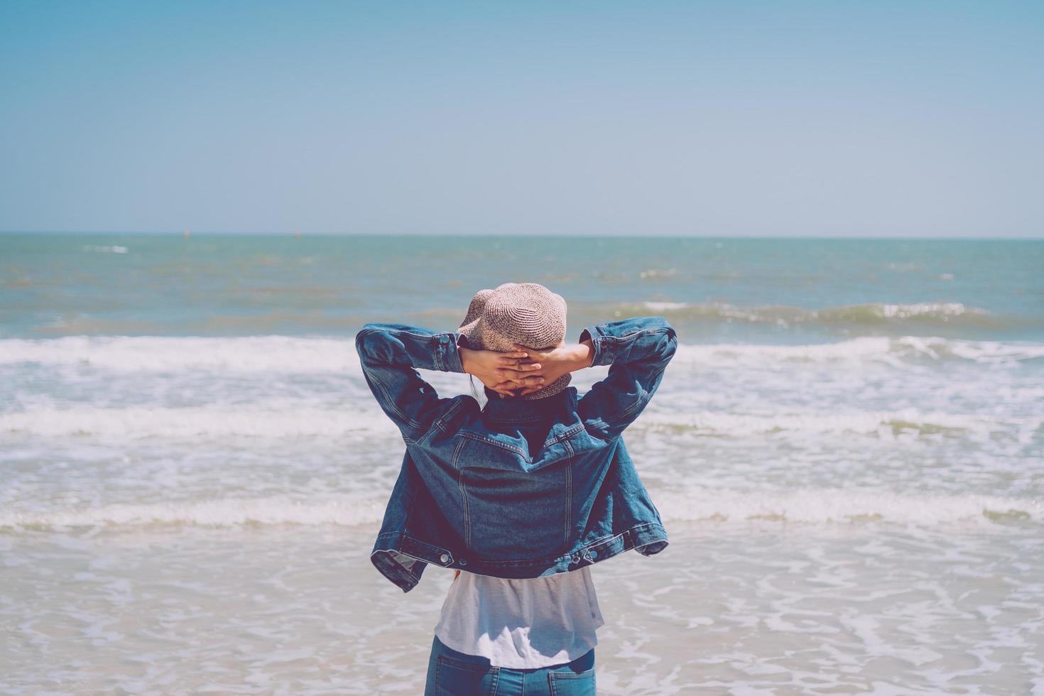 Woman raises hands up to the sky at the ocean photo