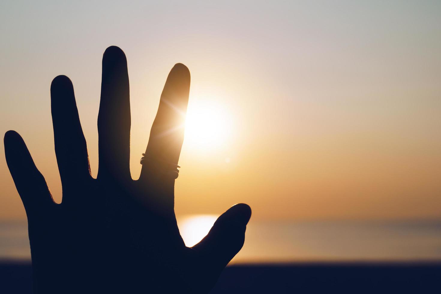 Hand silhouette reaches out to sunset sky photo