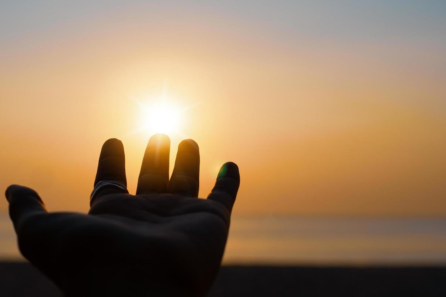 la silueta de la mano se extiende al cielo del atardecer foto