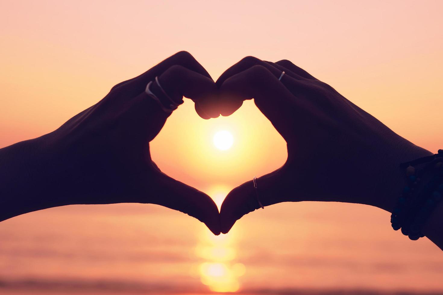 Woman's hand making a heart shape on sunset sky and bokeh background photo
