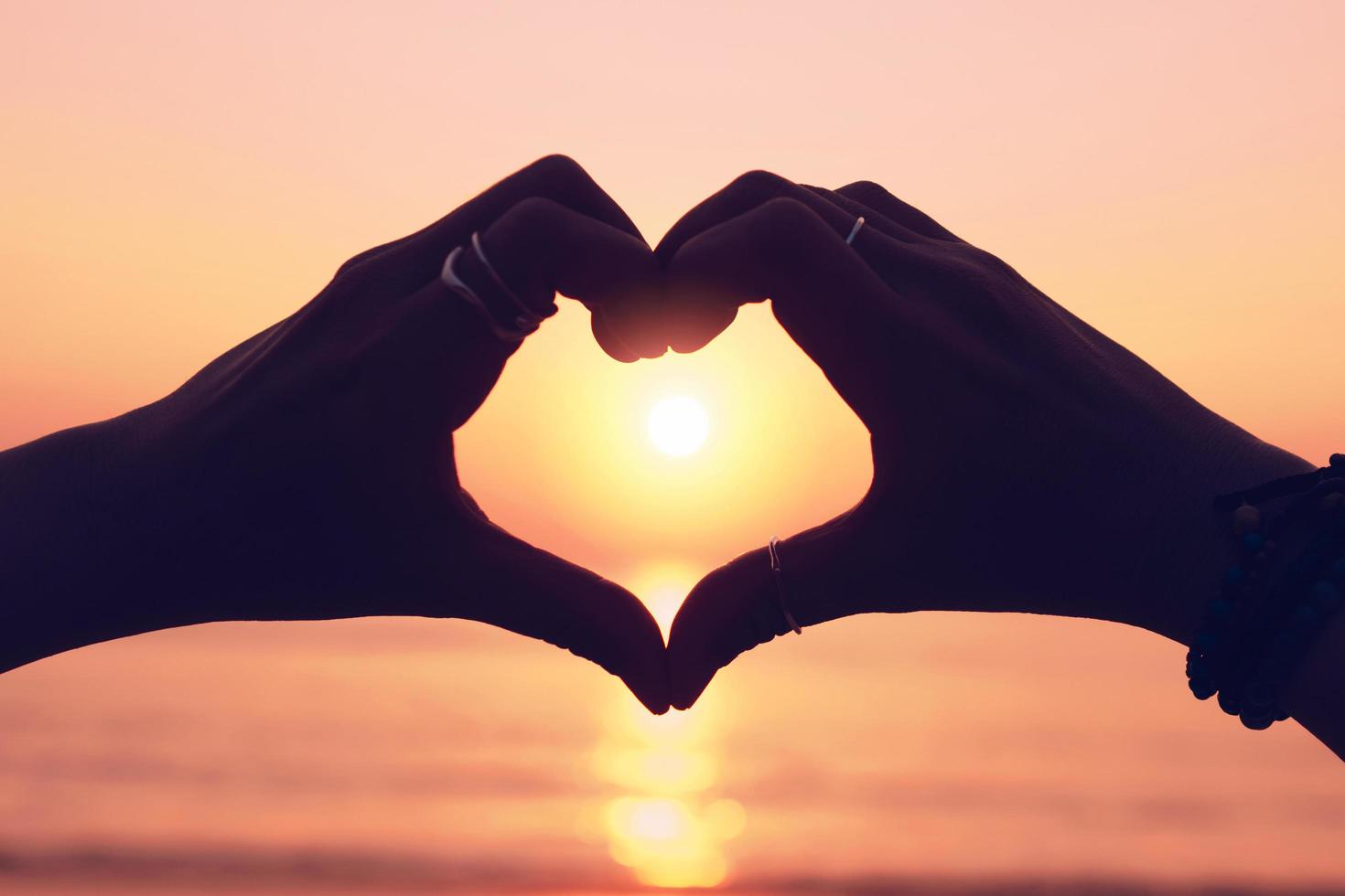 Mano de mujer haciendo una forma de corazón en el cielo del atardecer y fondo bokeh foto