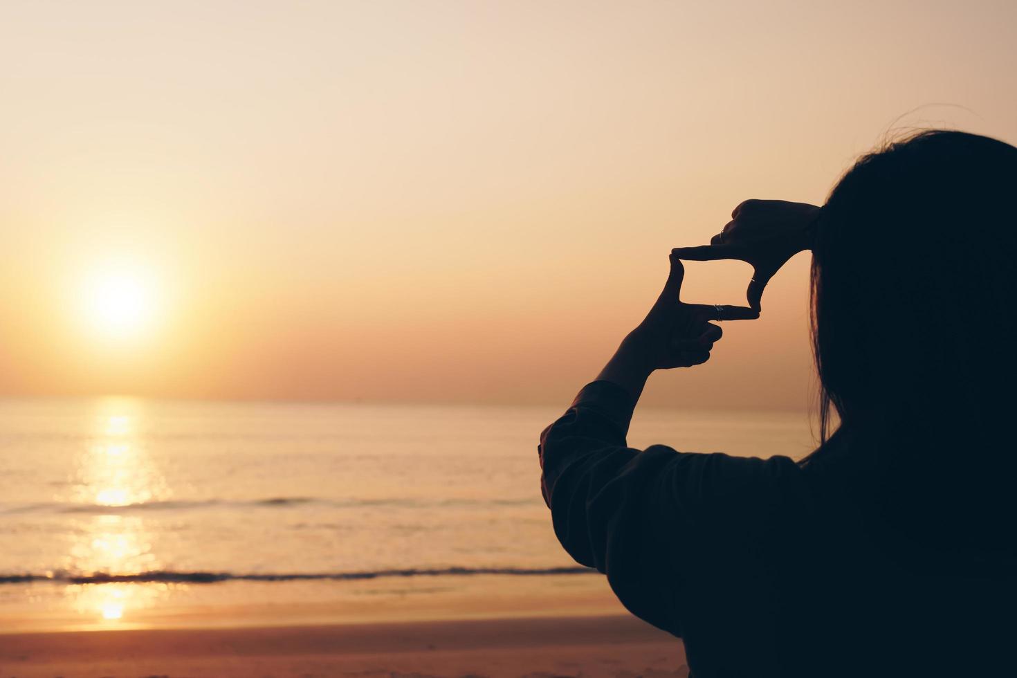 Selective focus of woman's hands making frame with sunrise photo