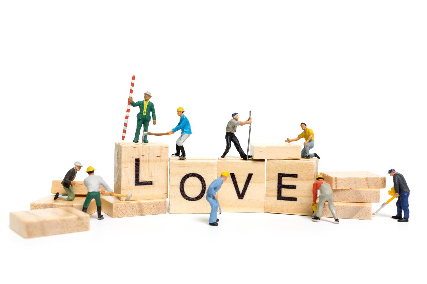 Miniature workers building the word Love on wooden blocks with a white background, Valentine's Day concept photo
