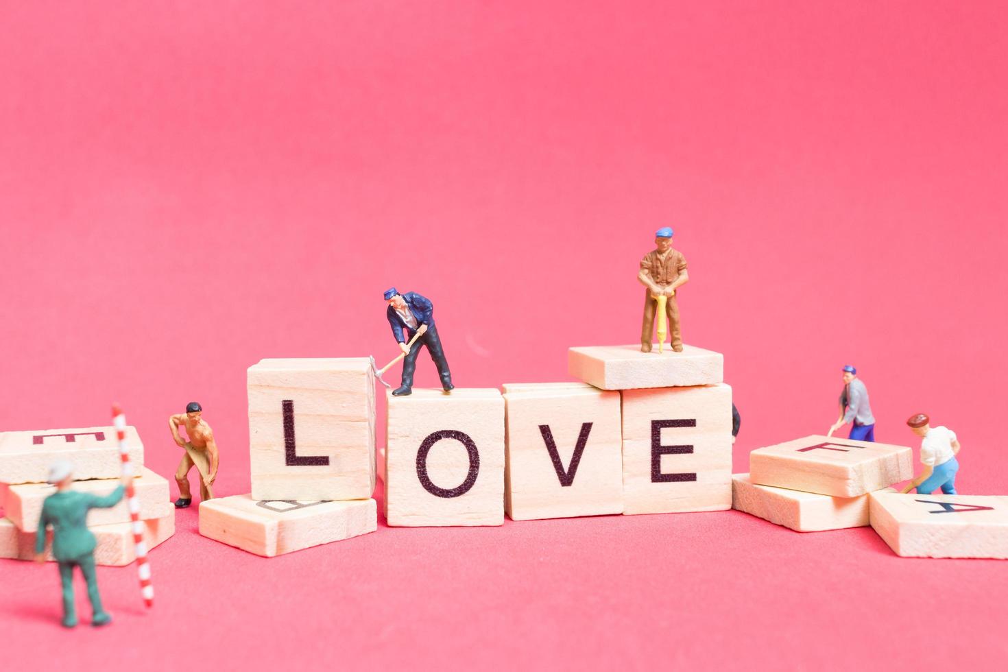 Miniature workers building the word Love on wooden blocks with a pink background, Valentine's Day concept photo