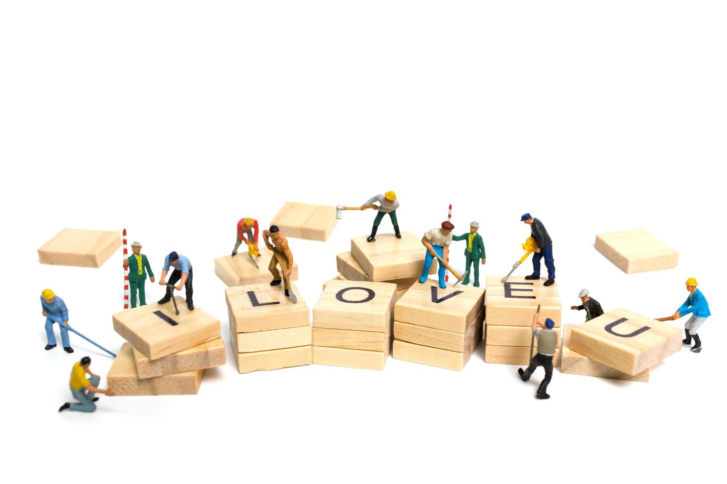 Miniature workers building the word Love on wooden blocks with a white background, Valentine's Day concept photo