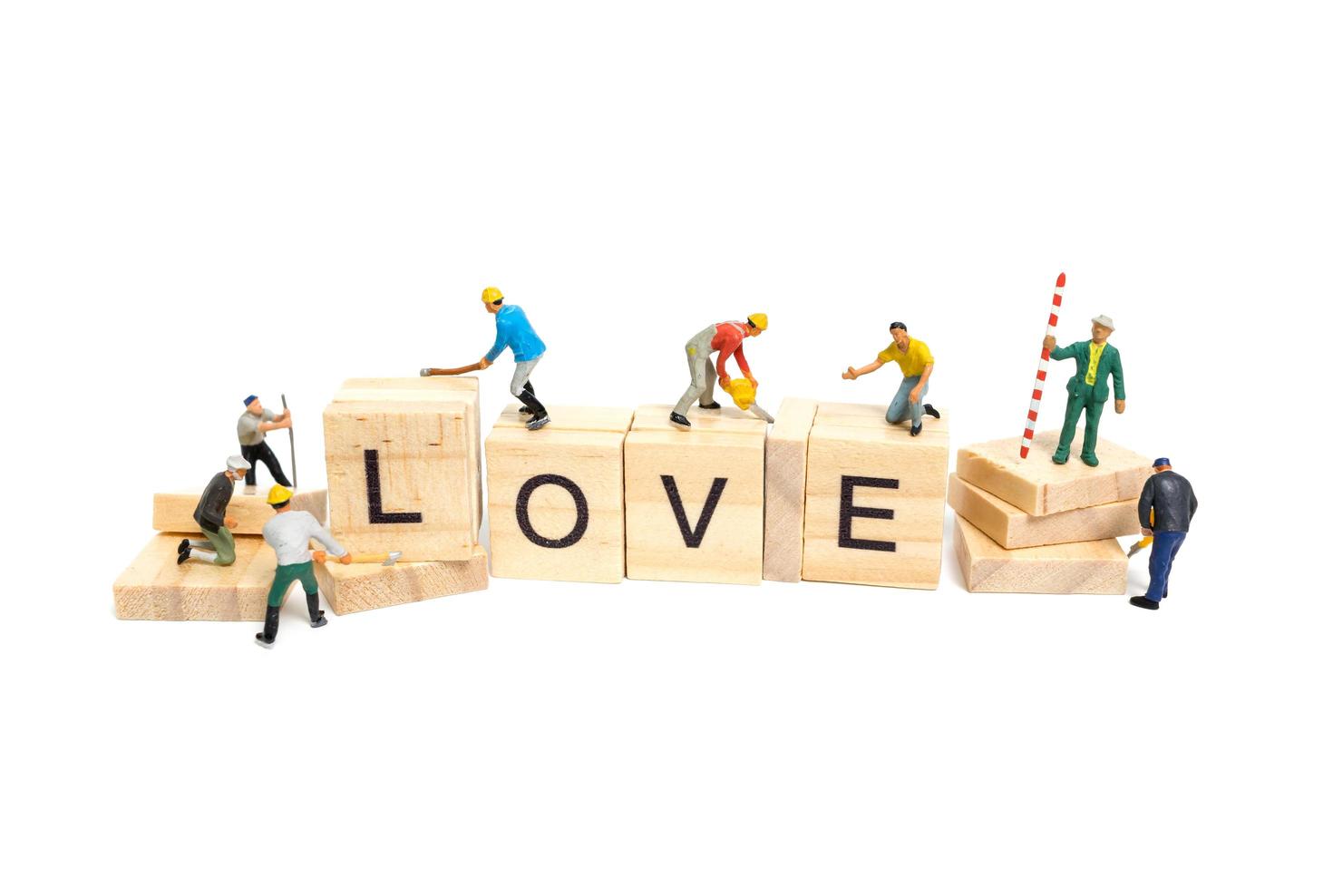 Miniature workers building the word Love on wooden blocks with a white background, Valentine's Day concept photo