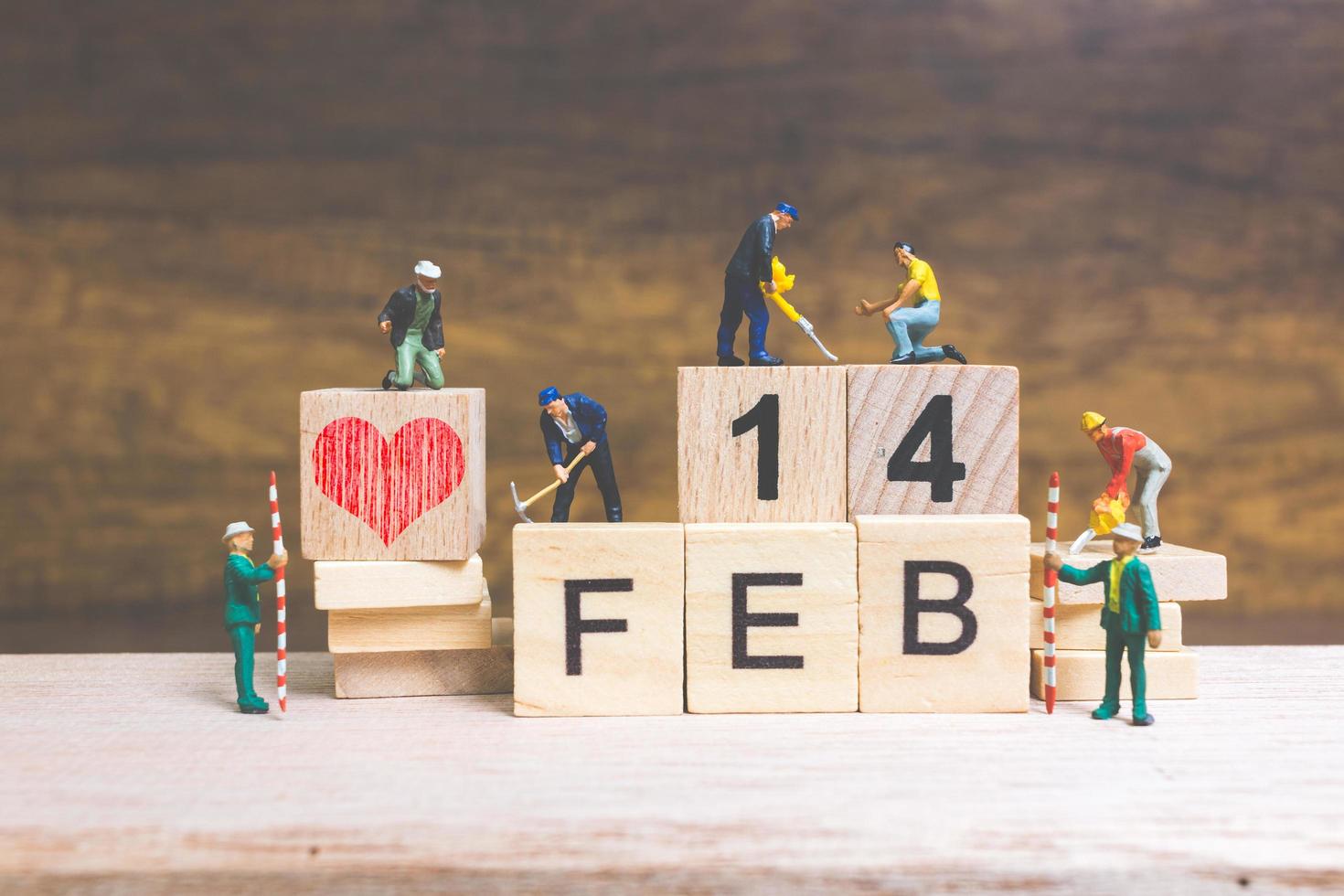 Trabajadores en miniatura construyendo las palabras y fechas para el día de San Valentín en bloques de madera con fondo de madera, concepto del día de San Valentín foto