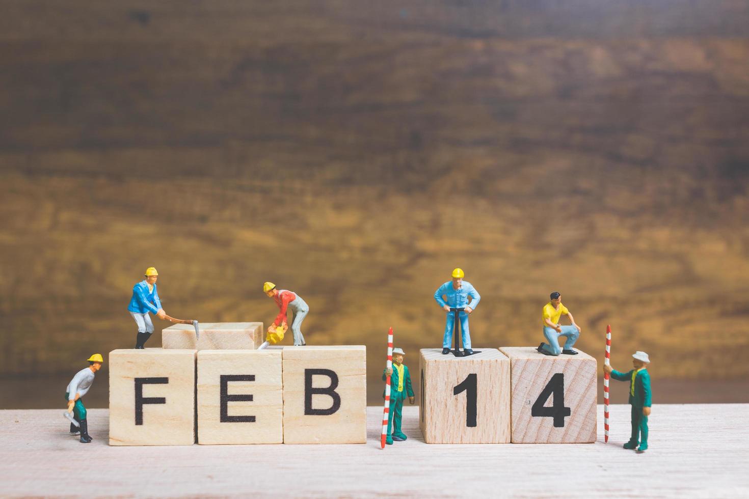 Trabajadores en miniatura construyendo las palabras y fechas para el día de San Valentín en bloques de madera con fondo de madera, concepto del día de San Valentín foto