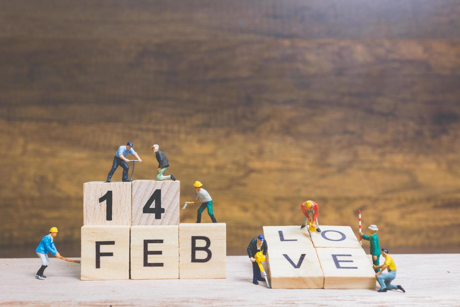 Trabajadores en miniatura construyendo las palabras y fechas para el día de San Valentín en bloques de madera con fondo de madera, concepto del día de San Valentín foto