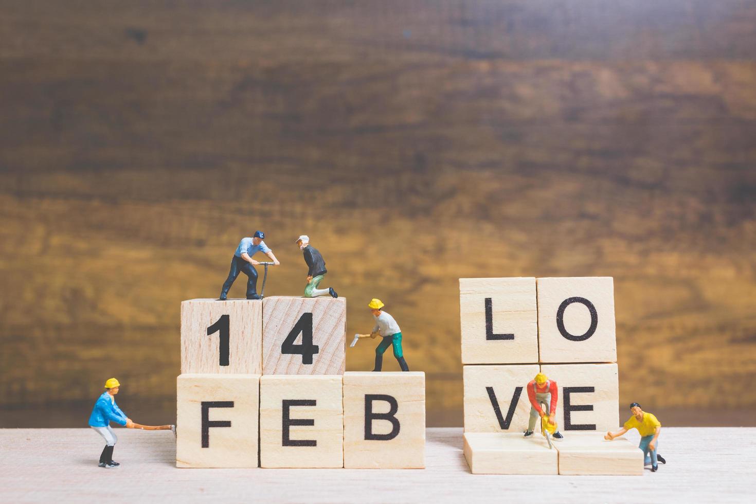 Trabajadores en miniatura construyendo las palabras y fechas para el día de San Valentín en bloques de madera con fondo de madera, concepto del día de San Valentín foto