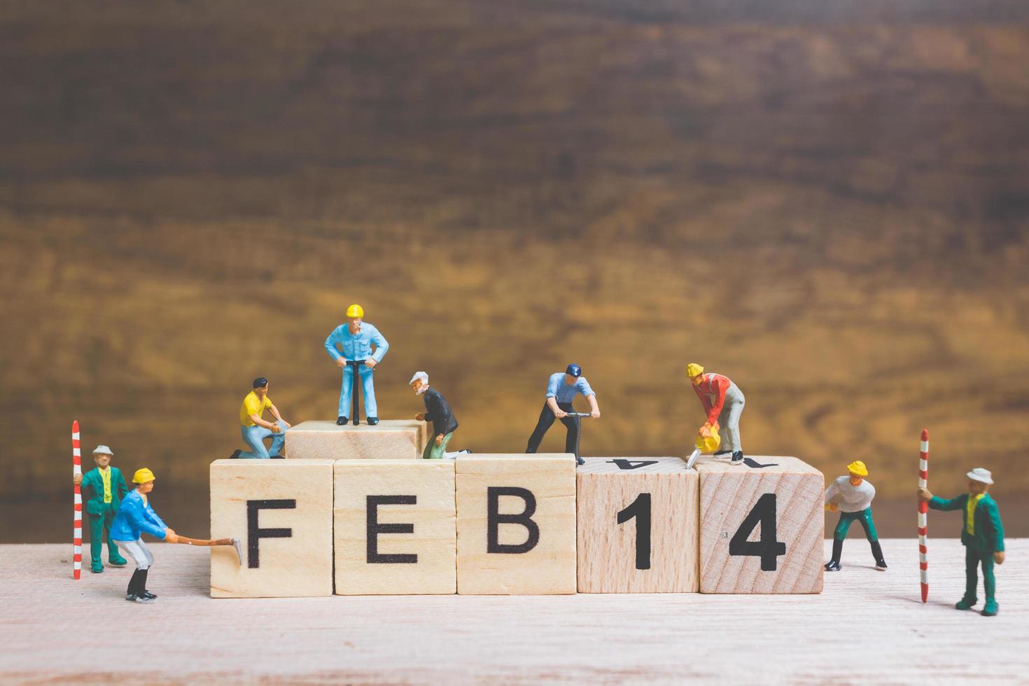 Miniature workers building the words and dates for Valentine's Day on wooden blocks with wooden background, Valentine's Day concept photo