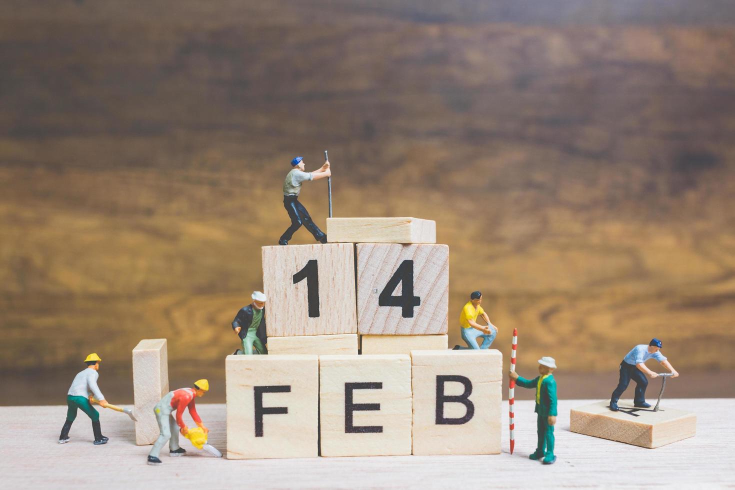 Trabajadores en miniatura construyendo las palabras y fechas para el día de San Valentín en bloques de madera con fondo de madera, concepto del día de San Valentín foto