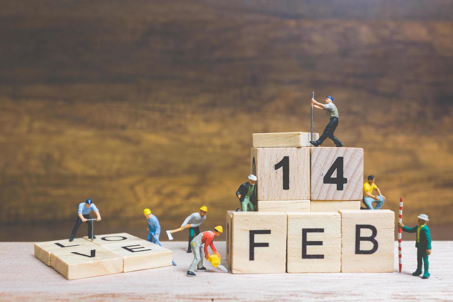 Trabajadores en miniatura construyendo las palabras y fechas para el día de San Valentín en bloques de madera con fondo de madera, concepto del día de San Valentín foto